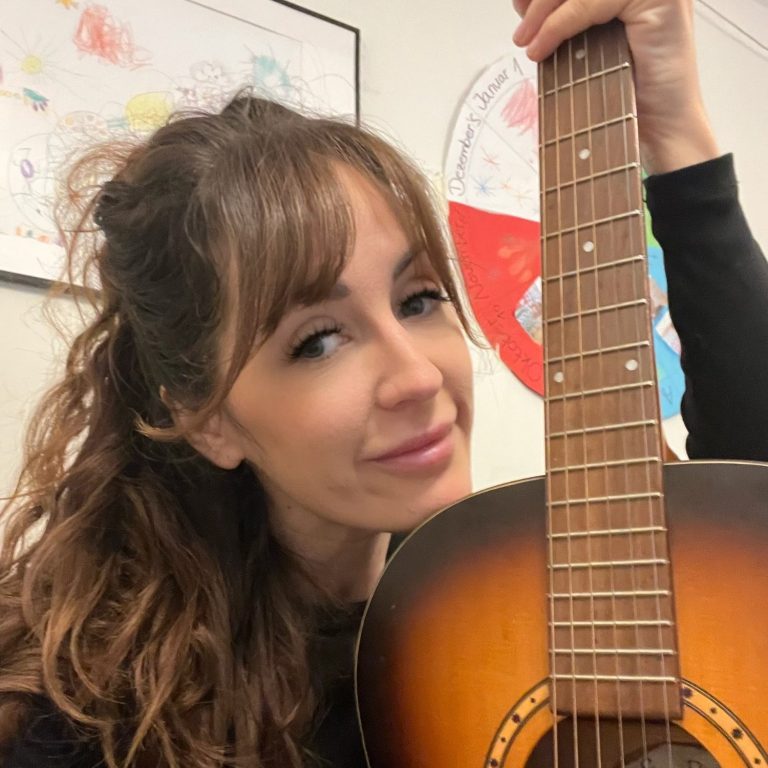 Frau hält eine Gitarre und lächelt in die Kamera.