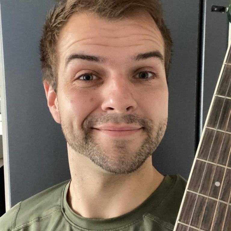 Lächelnder junger Mann hält eine Gitarre in der Hand.