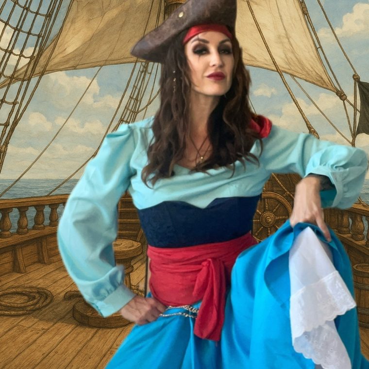 Eine Frau in Piratenkleidung steht auf einem Schiff mit Segeln im Hintergrund.