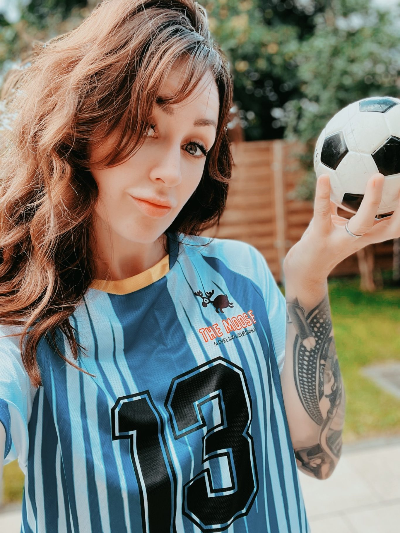 Kinderanimation, Partyspiele Hamburg Frau mit langen Haaren, trägt ein Fußballtrikot und hält einen Fußball in der Hand.